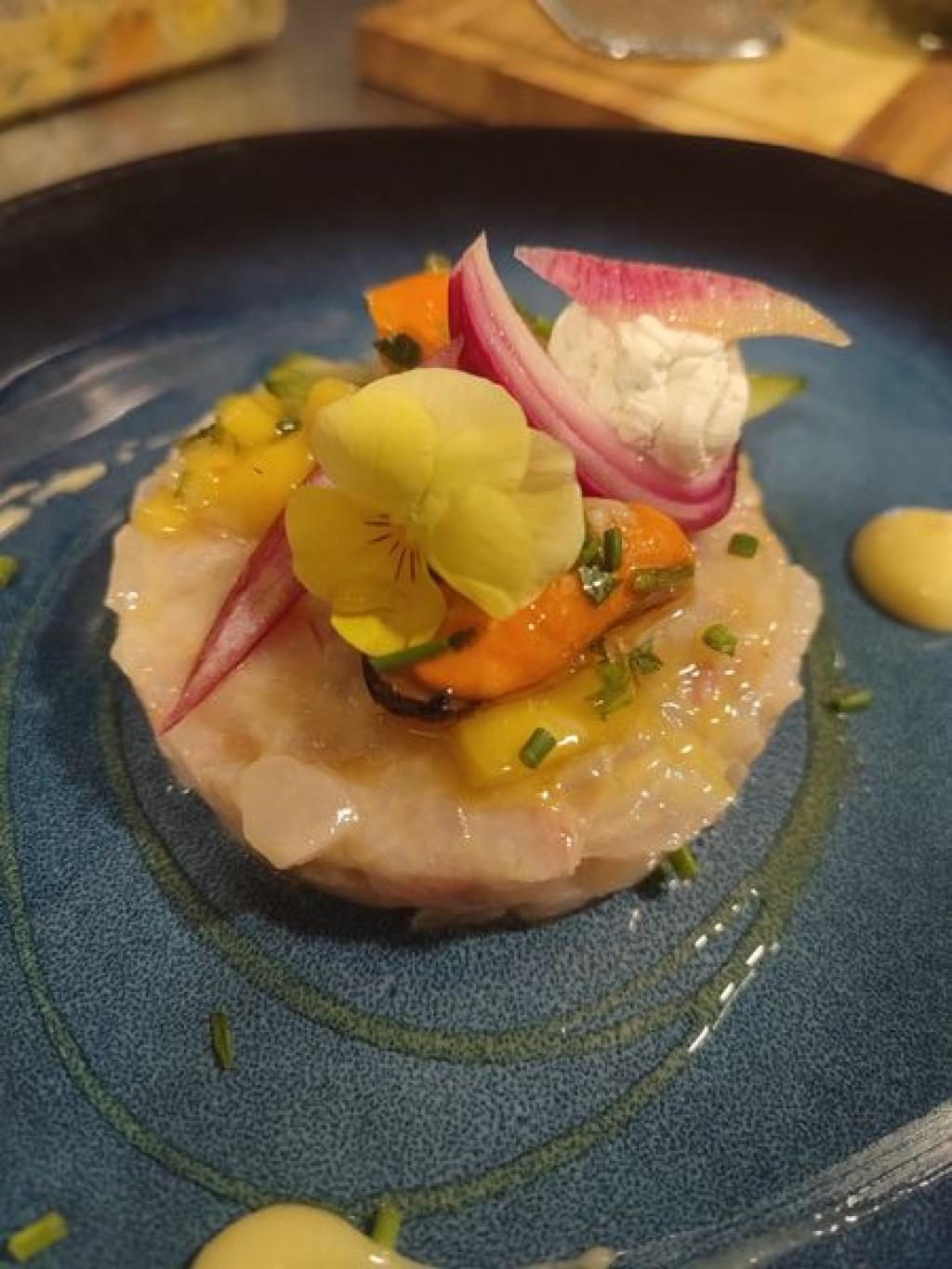 Un dessert dressé en assiette bleue, avec une glace jaune et des fruits