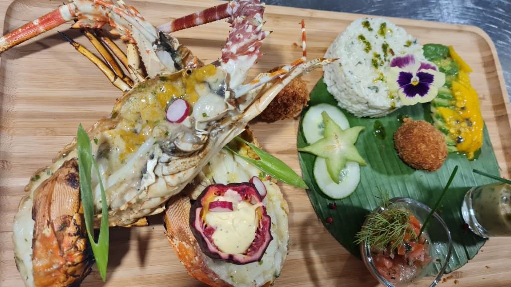 Un plateau antillais : crustacé, accras, légumes et fleurs comestibles, dressés sur une planche en bois