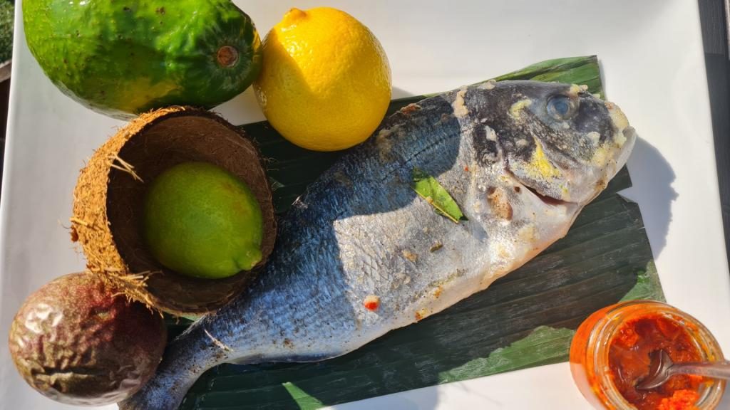 Une daurade posée sur une feuille de bananier, avec citrons verts et noix de coco